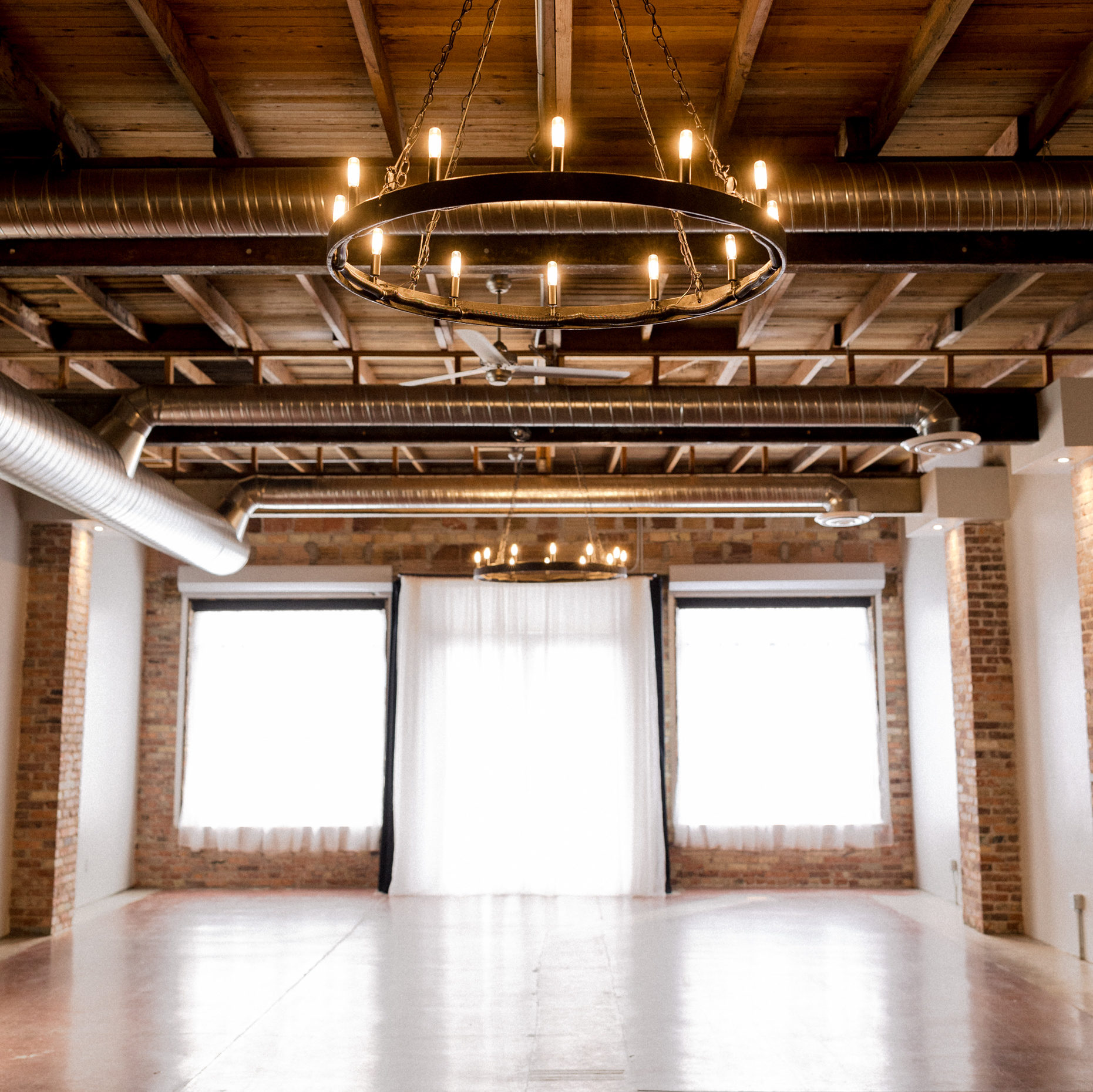 A large empty space with floor to ceiling windows, brick walls, and light flooding into the space.