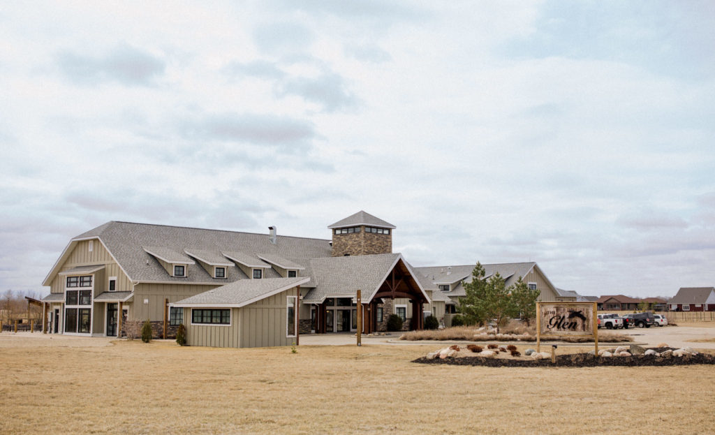 A large building with an open field surrounding it and a big entrance into it in an impressive display of modern rustic architecture.